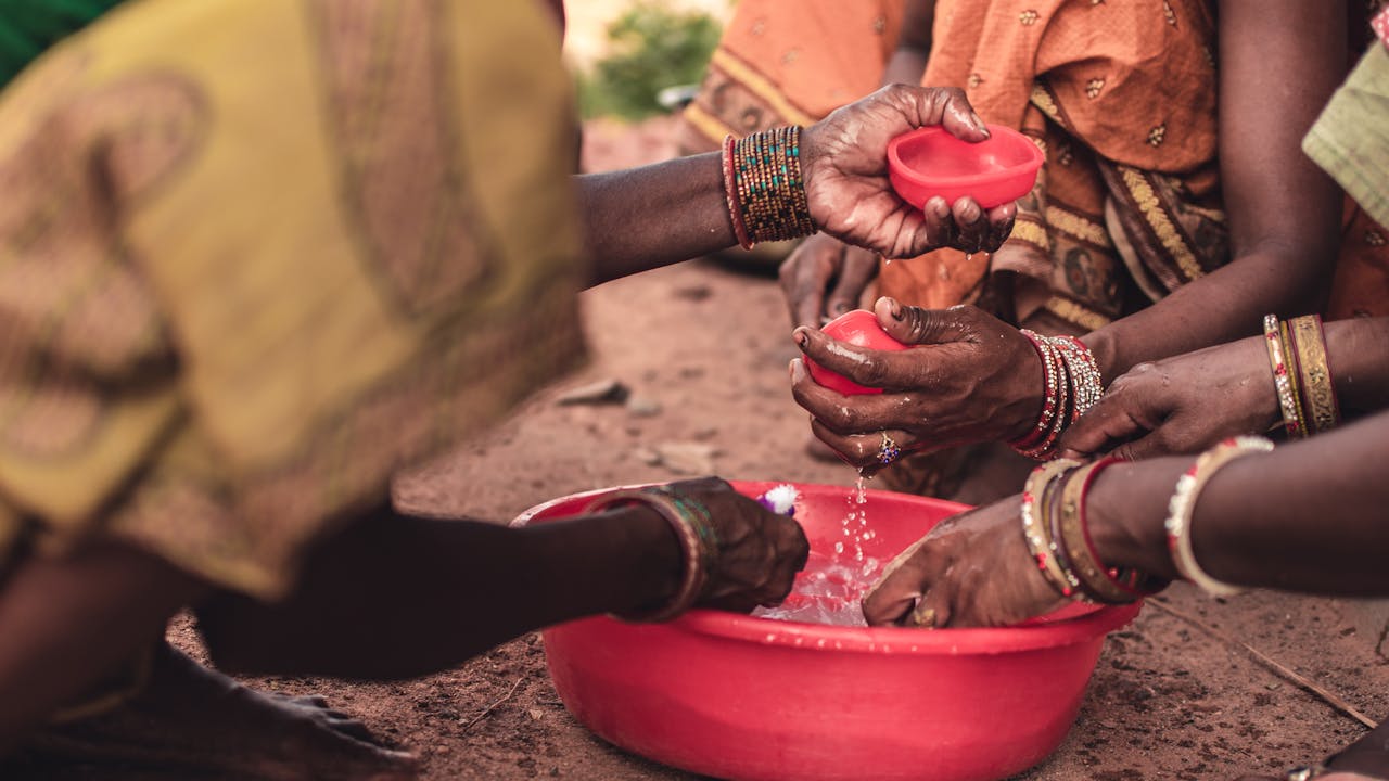 South Asian women washing hands with bowls, showcasing traditional wear and cultural practices in Odisha, India.